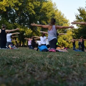 Group of adults practicing yoga outdoors in a park surrounded by trees.